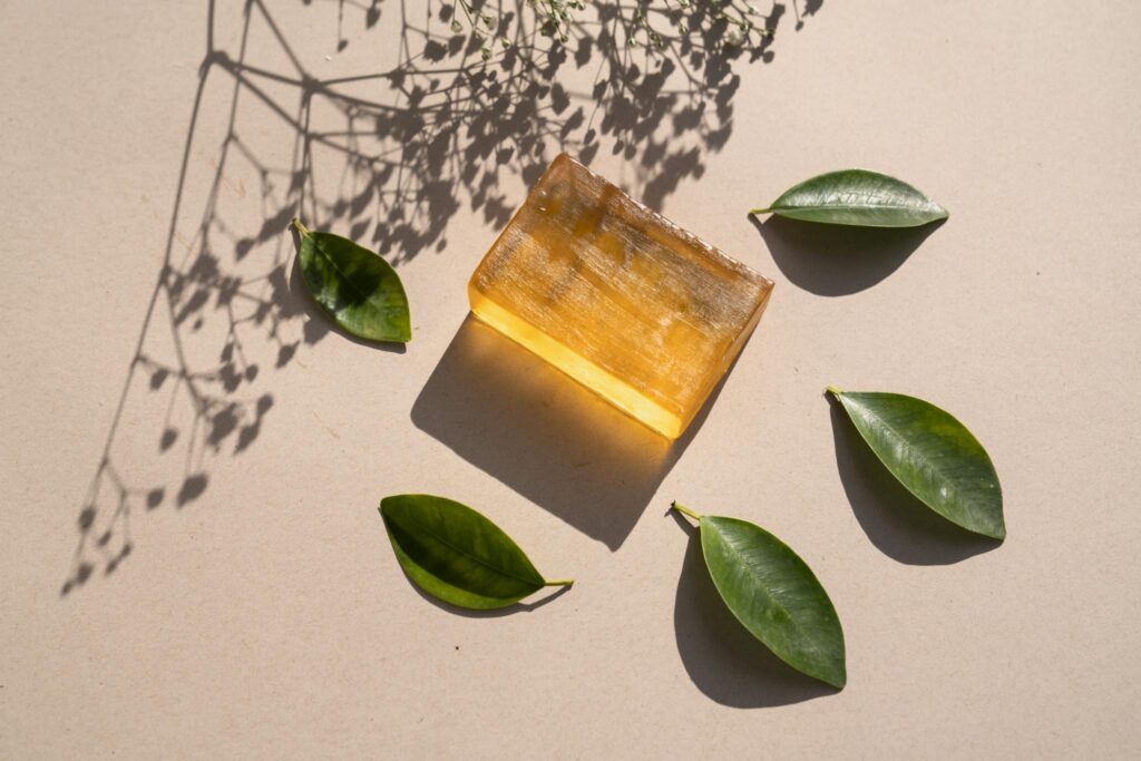 Flat lay of a natural soap bar with green leaves and shadows on a beige surface.